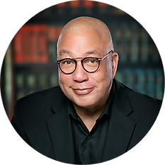 Smiling man with glasses and dark shirt standing in front of a bookcase