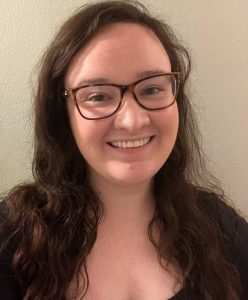 A beautiful winsome woman with long brown hair, tortoiseshell glasses, and a warm full smile