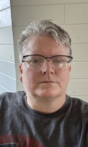 A woman with short salt and pepper hair, wearing glasses looking directly into the camera